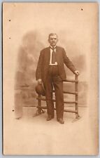 Cartão postal antigo RPPC retrato de um cavalheiro segurando chapéu perto de cerca de madeira, usado comprar usado  Enviando para Brazil