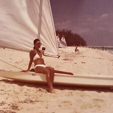 Foto a color vintage de mujer con bikini blanco sentada tabla de windsurf playa arena segunda mano  Embacar hacia Argentina